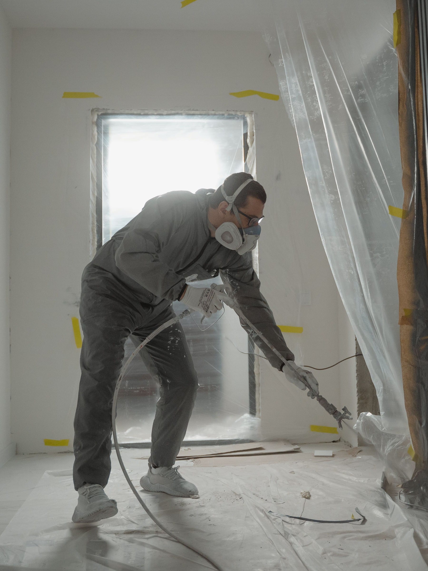 Peintre en combinaison et masque au pistolet dans une pièce en cours de rénovation