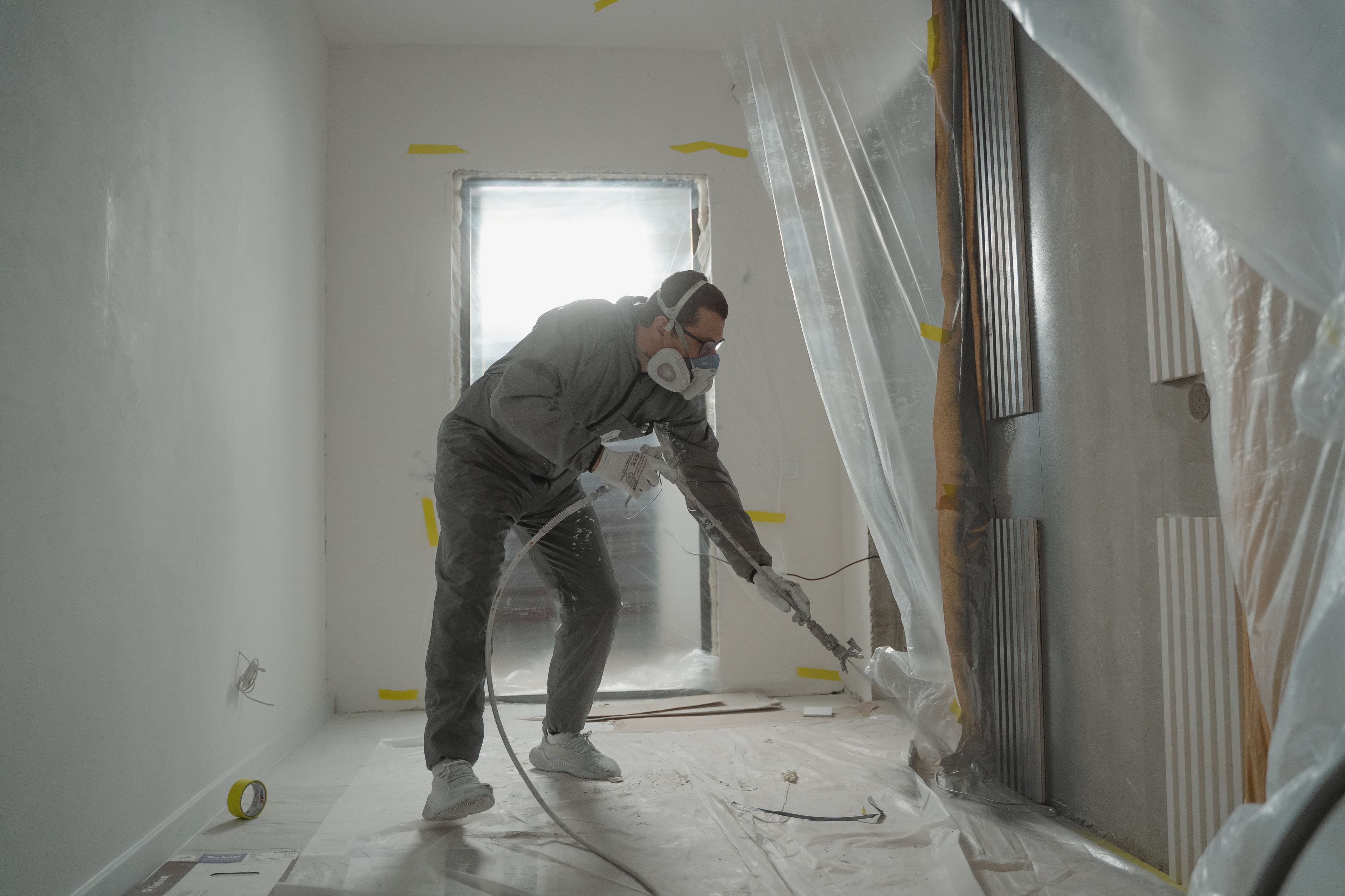 Peintre en combinaison et masque au pistolet dans une pièce en cours de rénovation